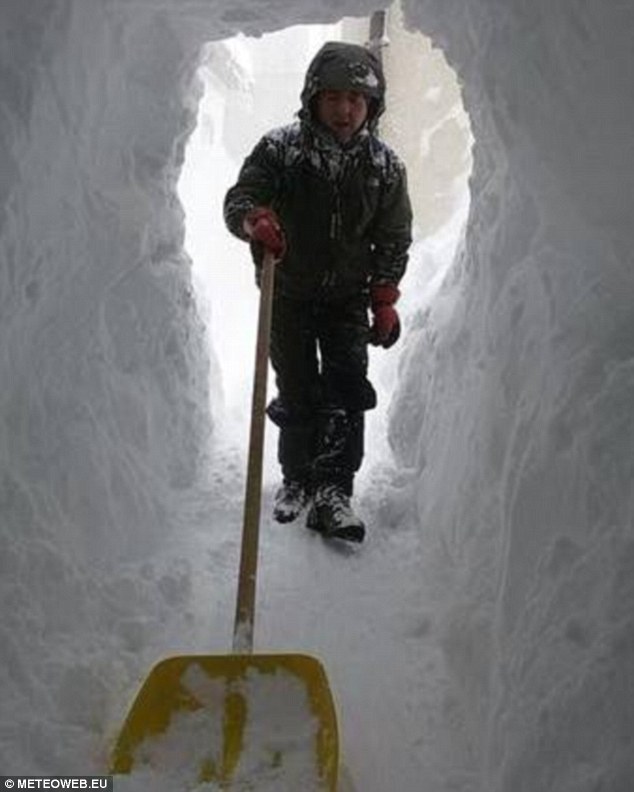 A man digs a tunnel as high as himself using a snow shovel as he creates a pathway from his home